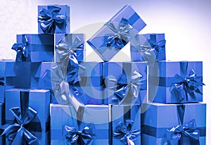 A lot of blue gift boxes with holiday ribbons on a light wall background. A mountain of gifts in bright festive packaging