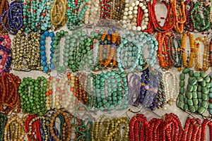 Lot of bright multi-colored bracelets made of balls of stones lying on the white surface of the table.  handmade