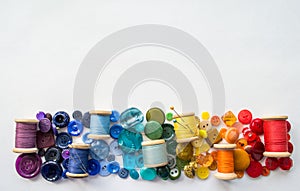 A lot of buttons and reels with colorful threads, laid out on a white background in the colors of the rainbow. Copy space