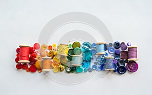 A lot of buttons and reels with colorful threads, laid out on a white background in the colors of the rainbow. Copy space