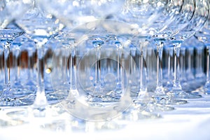 A lot of clean crystal glasses on white tablecloth prepared for big party. Blurred. Catering and restaurant utensils