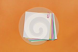 A lot of colored blank paper fastened pink paperclip on orange background