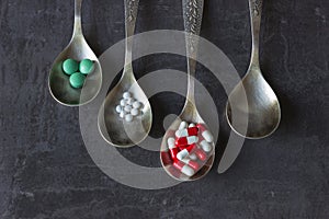 A lot of colored pills and medicines, vitamins, capsules in a spoon on a dark background.