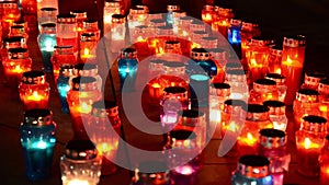 A lot of colorful candles burning at cemetery at night. Votive candles glows on grave. All saints day. Prayer lighted candles in a