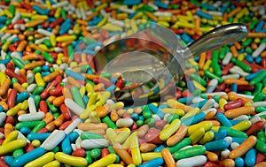 A lot of colorful candy drops in the form of capsules with a metal scoop for sale by weight. Sweet bright background