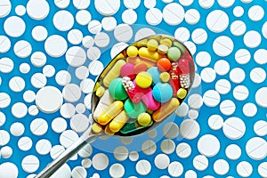 A lot of colorful pills in spoon on a blue background