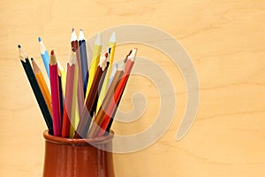 A lot of colorful sharpened pencils are in the cup on the wooden background