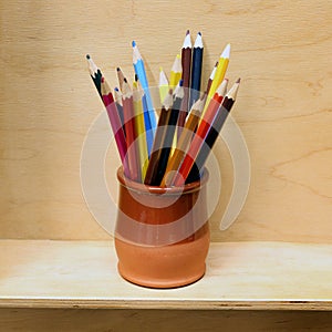 A lot of colorful sharpened pencils are in the cup on the wooden shelf