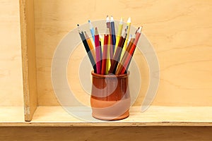 A lot of colorful sharpened pencils are in the cup on the wooden shelf