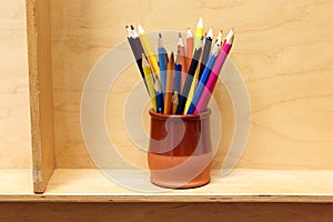 A lot of colorful sharpened pencils are in the cup on the wooden shelf