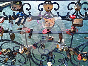 A lot of different locks on the forged fence of the bridge. As a symbol of strong love at a wedding. On the background of water, g