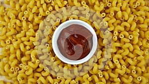 A lot of dry pasta as spirals and saucer with ketchup, rotate circle. Popular Italian and European cuisine.