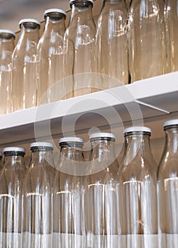 A lot of empty glass bottles with a white cap are on the shelf in a row. bottle for storing milk, juice, drinks and more.