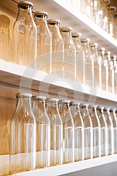 A lot of empty glass bottles with a white cap are on the shelf in a row. bottle for storing milk, juice, drinks and more.