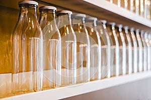 A lot of empty glass bottles with a white cap are on the shelf in a row. bottle for storing milk, juice, drinks and more.