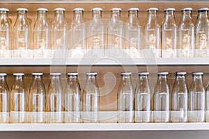 A lot of empty glass bottles with a white cap are on the shelf in a row. bottle for storing milk, juice, drinks and more.