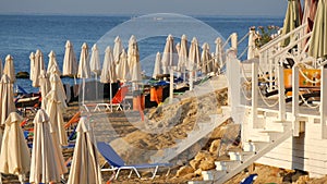 A lot of empty multi-colored sun loungers and folded beach umbrellas on resort beach by the sea, in a resort