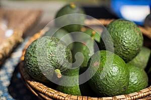 Lot of fresh avocados in a weaved basket with a blurred background