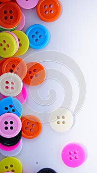 A lot of full spectrum multi colored vintage clothing plastic buttons randomly scattered on the white background - top view