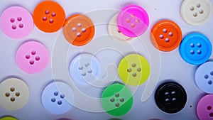 A lot of full spectrum multi colored vintage clothing plastic buttons randomly scattered on the white background - top view