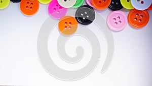 A lot of full spectrum multi colored vintage clothing plastic buttons randomly scattered on the white background - top view