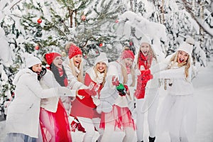 A lot of girls open a bottle of champagne violently in the winter new year`s forest.Girls in red and white clothes with new year