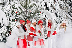 A lot of girls open a bottle of champagne violently in the winter new year`s forest.Girls in red and white clothes with new year