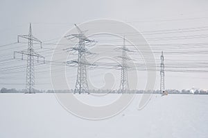 A lot of high voltage power, electrical energy transmission tower overhead line masts in winter with lots of snow on the fields