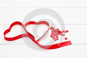 A lot of little red hearts and a red ribbon in the form of heart on white wooden background.