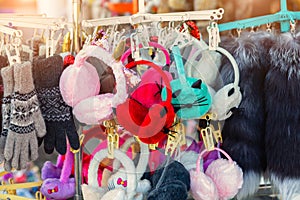 Lot of many multicolored bright fluffy warm winter fur earphones and gloves hanged on rack at store display for sale. Cute cold