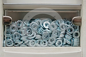 lot of metal washers in a transparent box. Storage of fasteners and parts in a cell