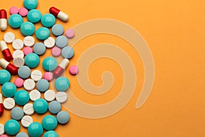 Lot of multicolored pills and tablets on orange background with free space for text or prescription