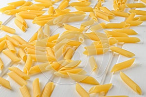 A lot of pasta is scattered on a white wooden table.