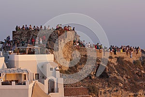 A lot of people on the walls of the ancient fortress of the Greek island of Santorini awaiting sunset.