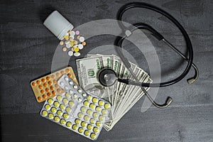 A lot of pills, a stethoscope and money on a dark table