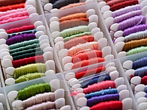 A lot of plastic bobbins with different colour embroidery threads in plastic sorting box