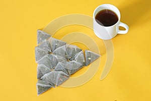 Lot of pyramid tea bags with green tea, with pieces of fruit, and white mug on yellow background. Pyramid shape. Ð¡oncept of