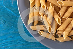 A lot of raw pasta penne on a patr of plate at blue wooden background photo