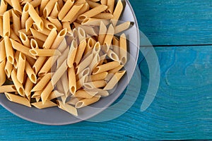 A lot of raw pasta penne on a patr of plate at blue wooden background photo