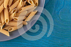 A lot of raw pasta penne on a patr of plate at blue wooden background photo