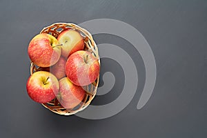 Lot of red fresh whole ripe apples full of vitamins lies in wooden wicker basket and old dark scratched concrete table on kitchen