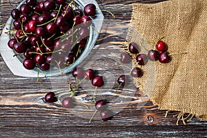 A lot of ripe red cherries on twigs lie in a glass plate on a dark blue wooden table