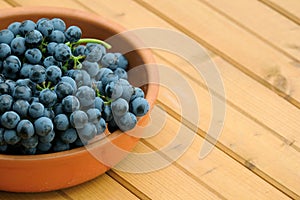 Lot of ripe red grape berries on bunch in brown round bowl on wooden table front view close up