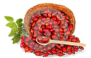 Lot of rose hips fell out of wicker basket nearby wooden spoon with berries isolated on white