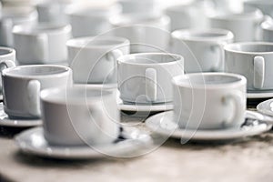 a lot of rows of pure white cups with plates for coffee or tea break