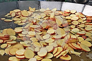 A lot of sliced potato slices are fried in big steel pan