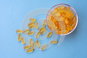 A lot of soft jelly capsules with fish oil as a source of Omega 3 in a transparent  bowl on blue background. Concept of health