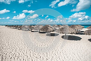 a lot of thatched sun shelters. Umbrellas stand in a row on sand at a resort on Varadero beach in Cuba