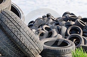 A lot of used tyres with green grass in one of against blue sky with white clouds