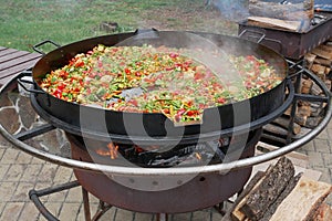 A lot of various sliced vegetables are fried in big steel pan